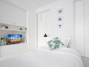 Quarto moderno com cama, guarda-roupa branco e estante com livros e objetos decorativos.