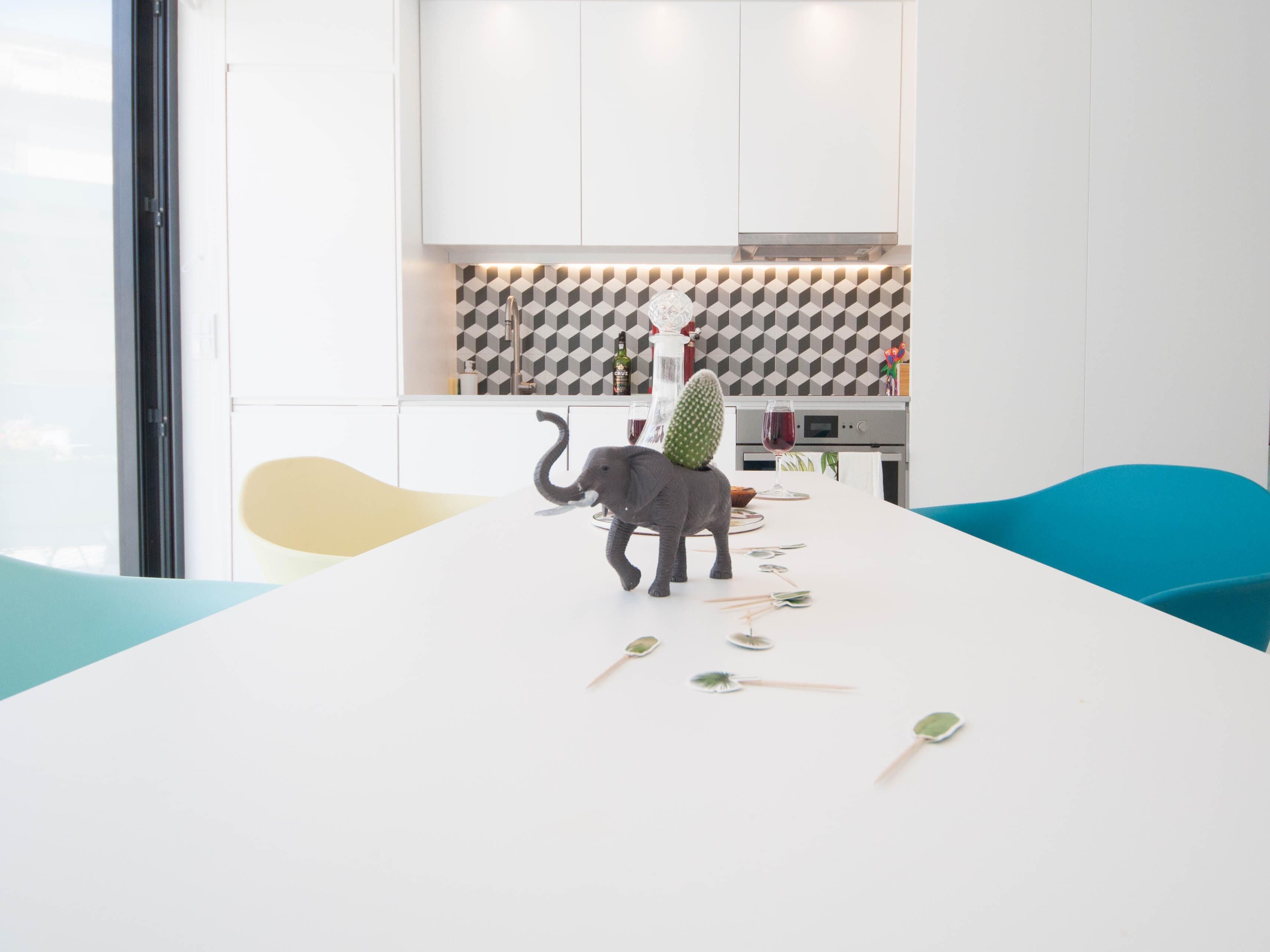 A modern kitchen with a white countertop, a cactus sculpture, and a dining area with blue chairs.