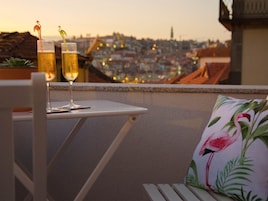 Una mesa con dos vasos de cerveza en un balcón con vista a un paisaje urbano al atardecer.