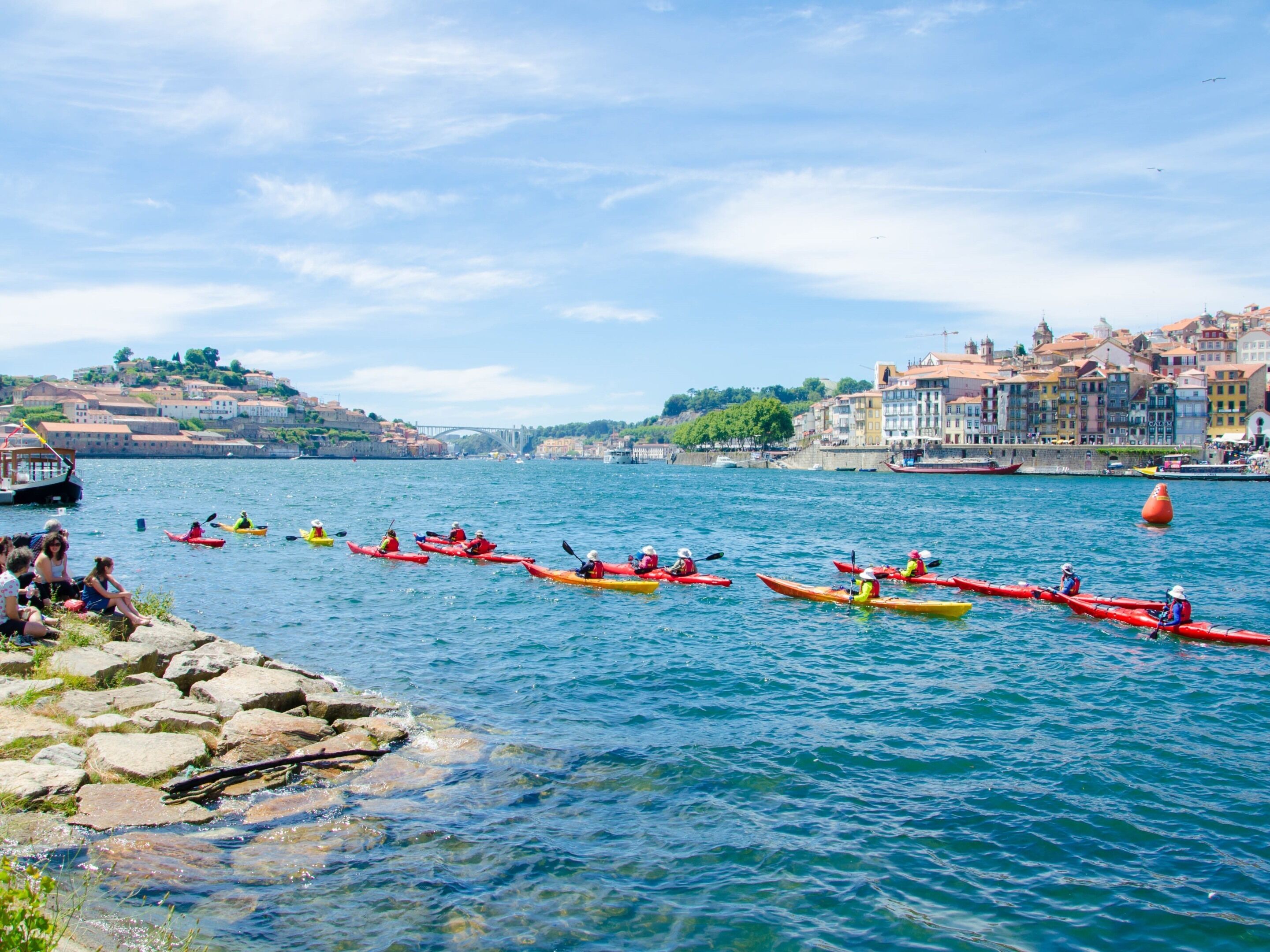 A waterfront scene with kayakers in red and yellow kayaks.