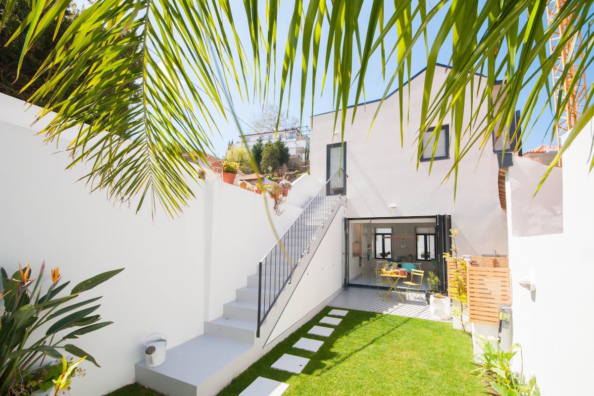 A modern house with a white exterior, a small front yard with a lawn and stepping stones, and a staircase leading to the entrance.