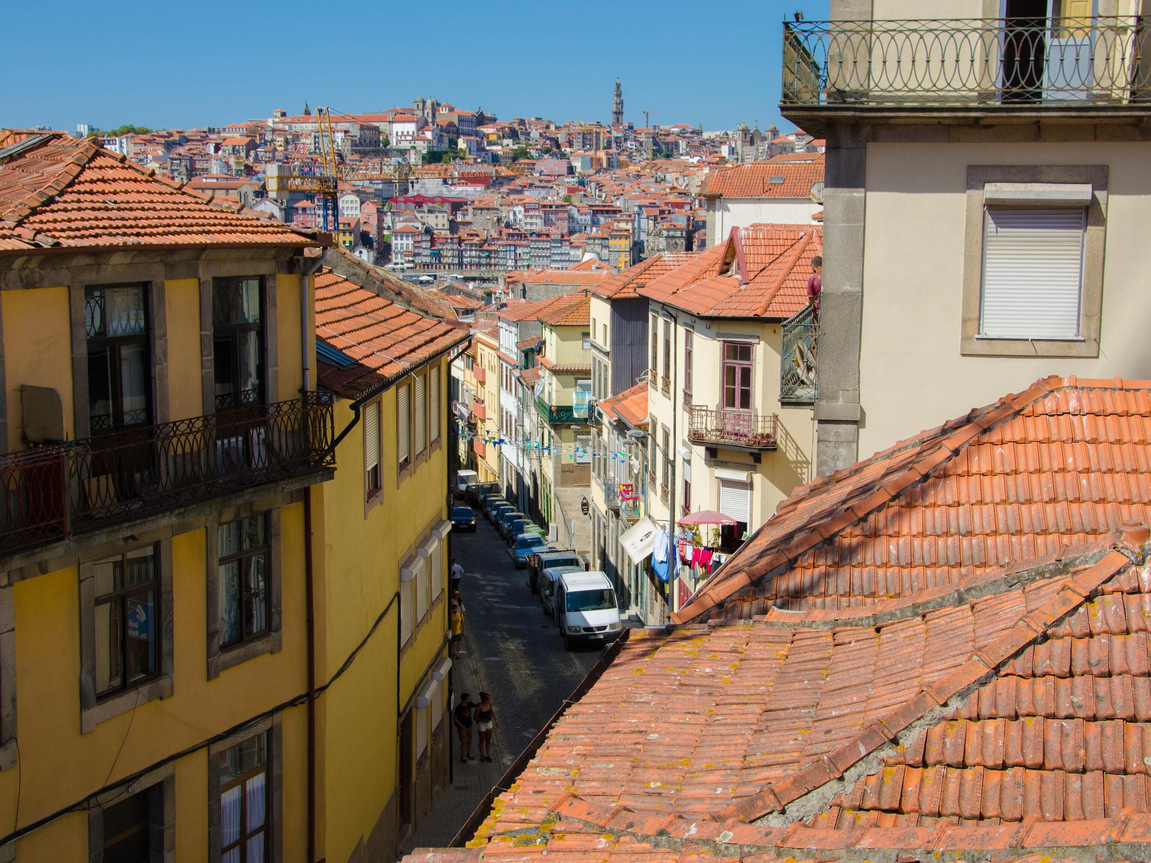 Una calle estrecha flanqueada por edificios coloridos, con una aguja de iglesia a la vista y una vista despejada del paisaje urbano en la distancia.