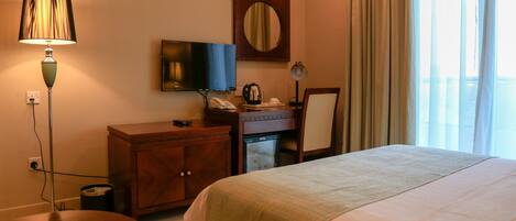 A hotel room with a bed, a desk with a computer, a television, a mirror, and a window with curtains.