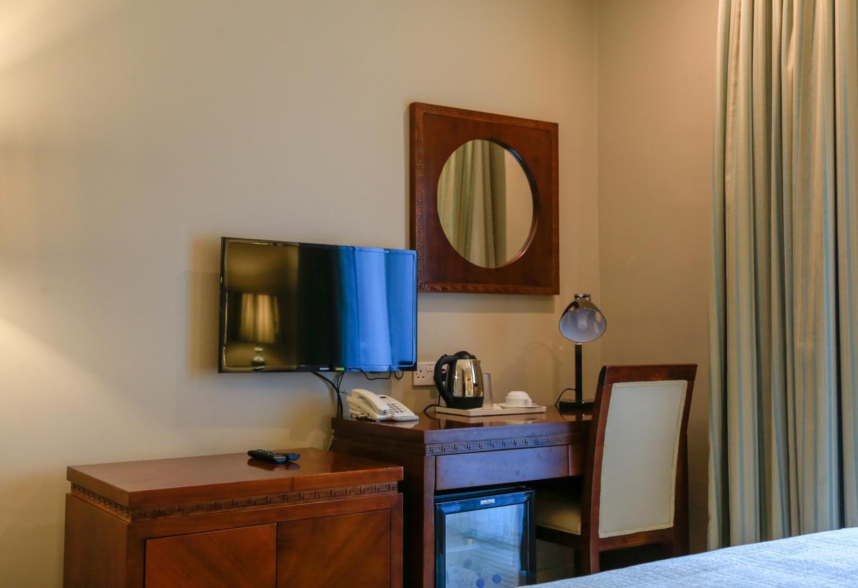 A hotel room with a bed, a desk with a telephone and a coffee maker, a television, and a mirror.