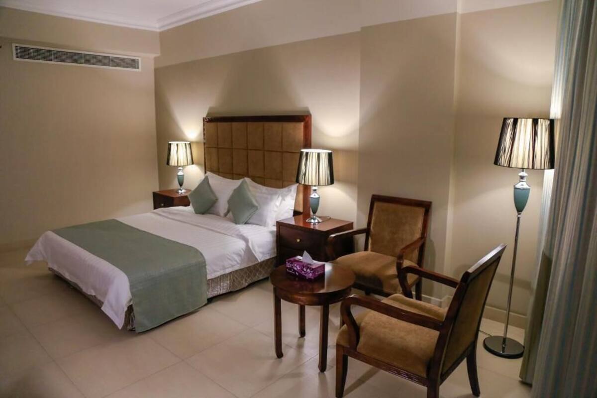 A hotel room with a bed, two bedside tables with lamps, a chair, and a floor lamp.
