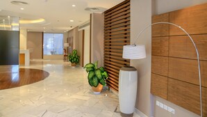 Un moderno vestíbulo de hotel con piso de mármol, paneles de madera, una recepción y plantas en macetas.