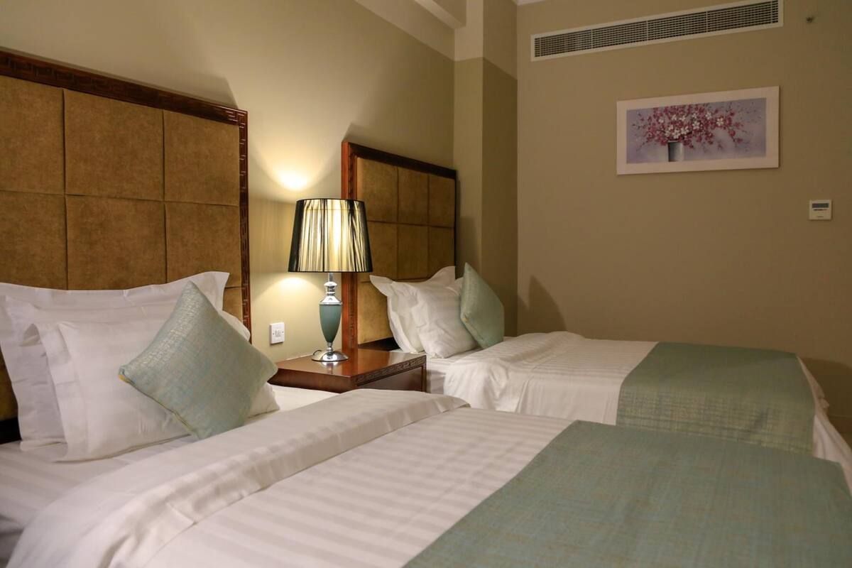 A hotel room with two beds, a nightstand with a lamp, and a wall-mounted painting.