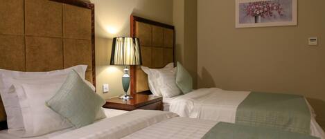 A hotel room with two beds, a nightstand with a lamp, and a wall-mounted painting.