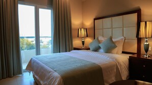 Una habitación de hotel con una cama grande, dos mesitas de noche con lámparas, vistas al exterior a través de una ventana y un balcón.