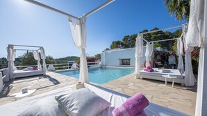 A poolside area with white lounge chairs, a small table, and a view of the pool and greenery. - Agroturismo Can Cosmi Prats (Santa Eulalia del Rio)