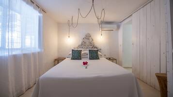 A bedroom with a large bed, two bedside tables, a chandelier, and a window with sheer curtains.