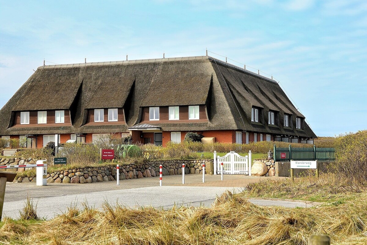 Un grand bâtiment traditionnel, doté d’un toit de chaume, qui ressemble probablement à un hôtel ou à une maison d’hôtes, avec une entrée en pierre et une enseigne indiquant qu’il s’agit d’un espace privé.