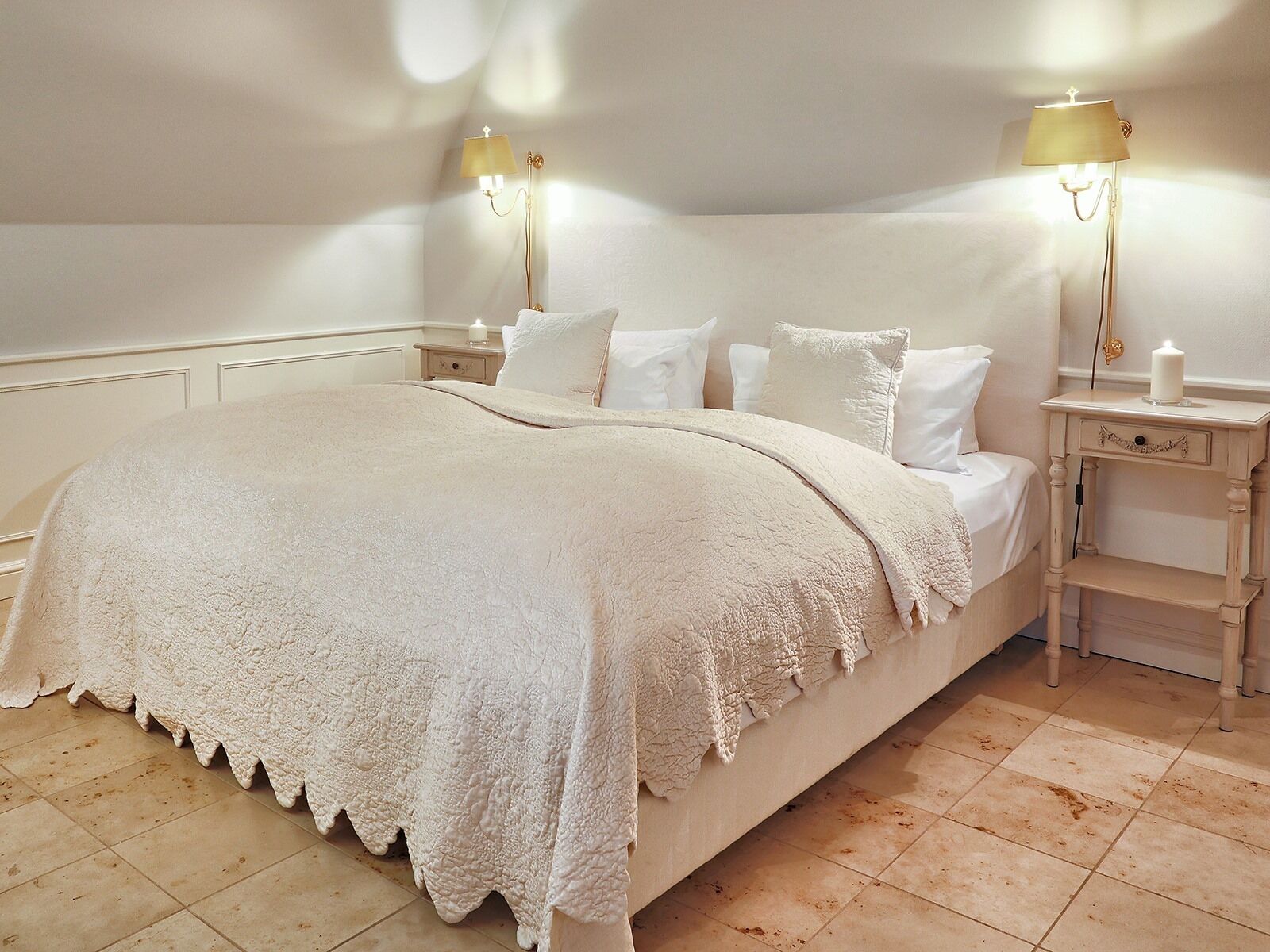 Un dormitorio con una cama grande, dos mesitas de noche, una mesilla auxiliar y una lámpara de pared.