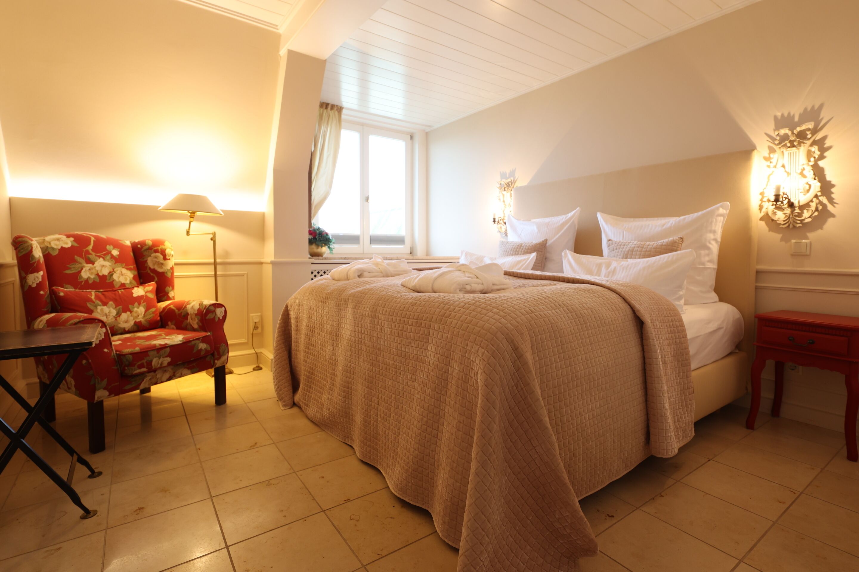 Une chambre à coucher avec un lit, une chaise, une lampe et une fenêtre.