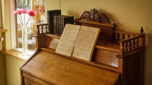 Een houten piano met bladmuziek, geplaatst naast een raam met een bloevas.