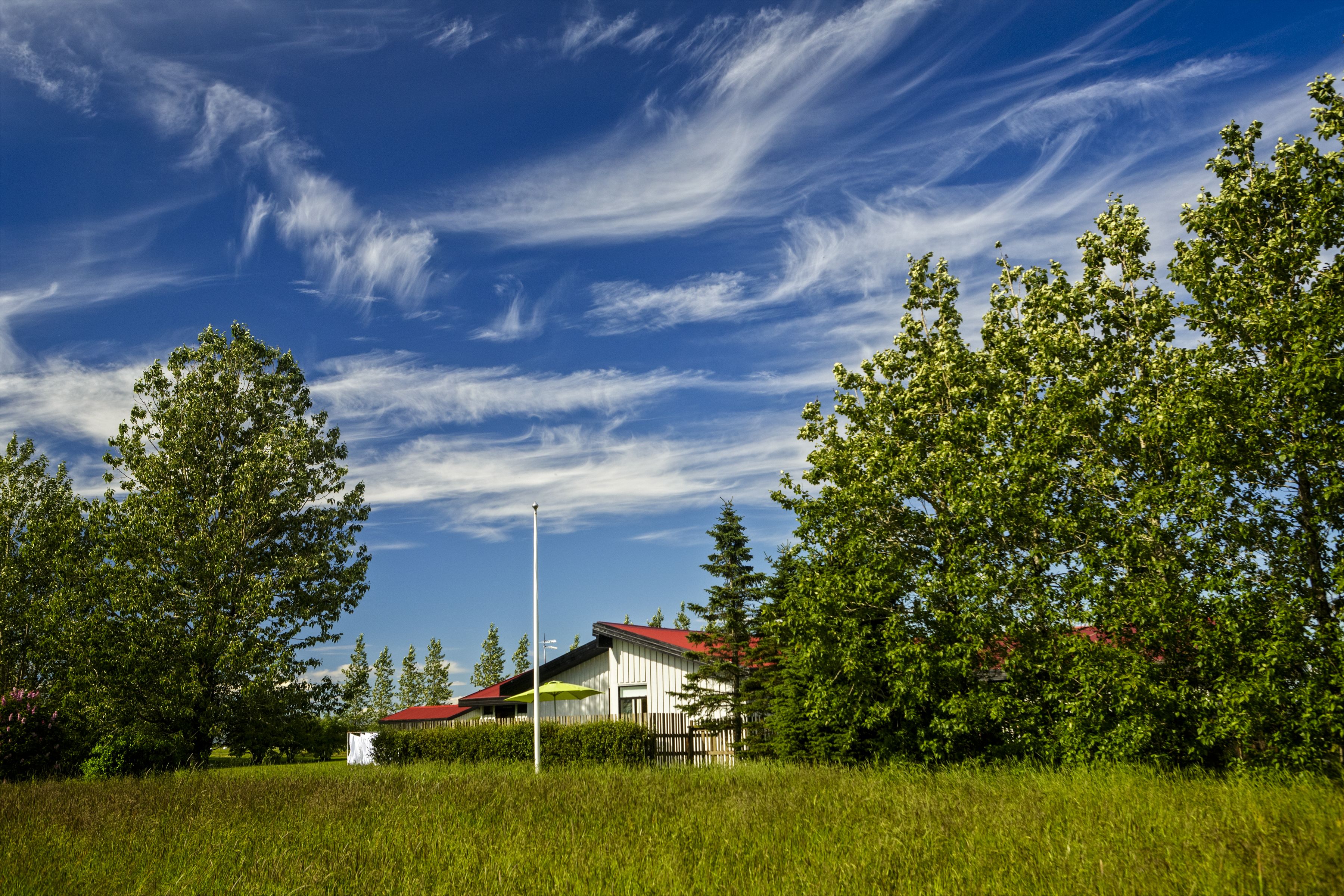A rural setting with a white building with a red roof, surrounded by lush green trees and grass.
