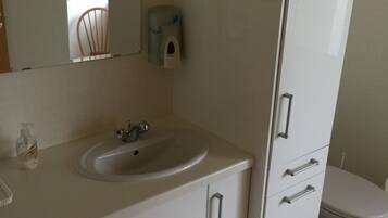 A bathroom with a white sink, mirror, and toilet. There is a soap dispenser on the wall and a bottle of hand soap on the counter.