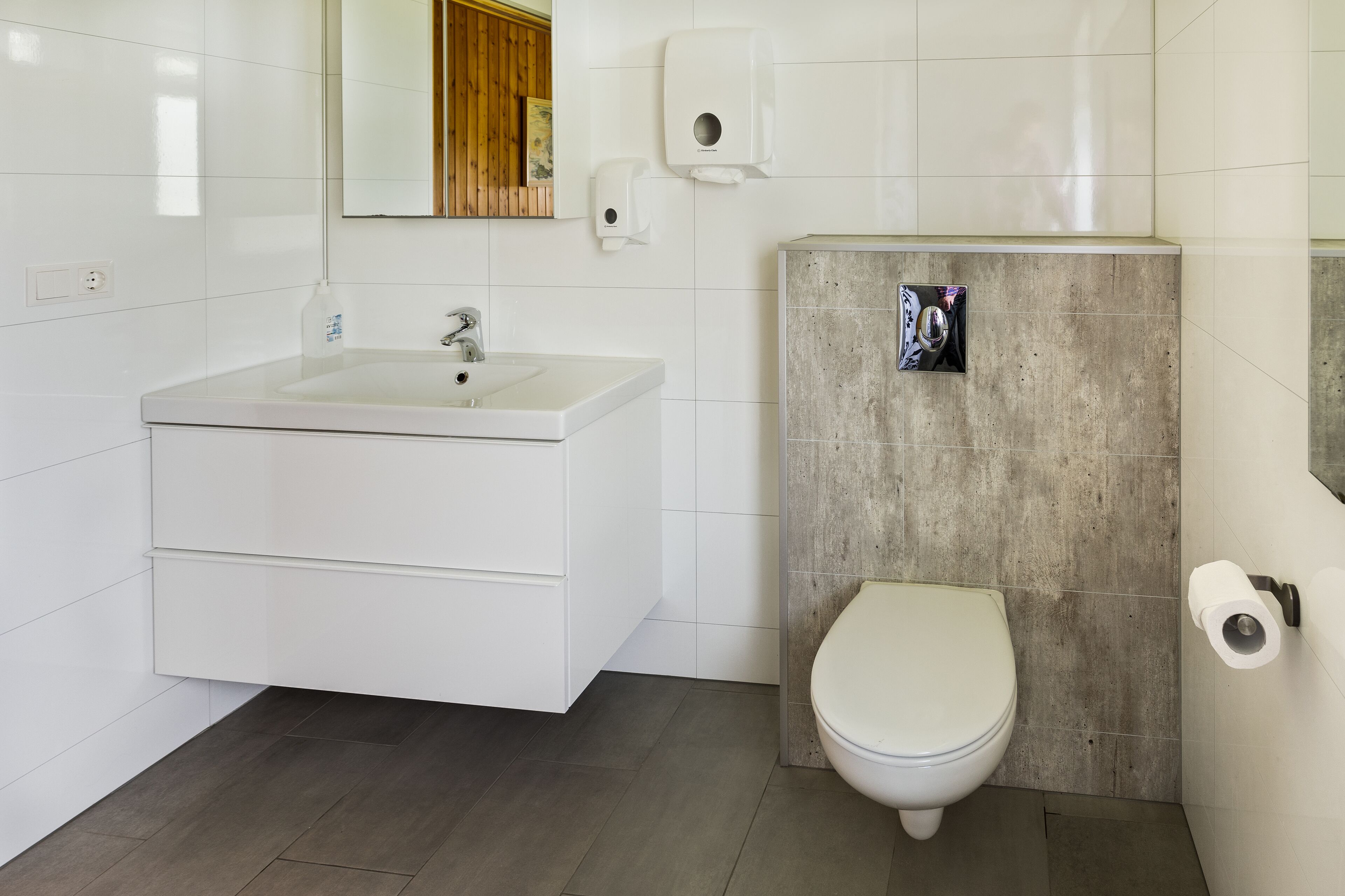 A modern bathroom with a white sink, a toilet, and a paper towel dispenser.