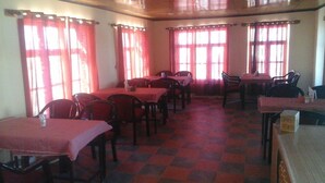 A dining area with tables and chairs, large windows with curtains, and a checkered floor pattern. - Lotus Camp and Restaurant (Leh)