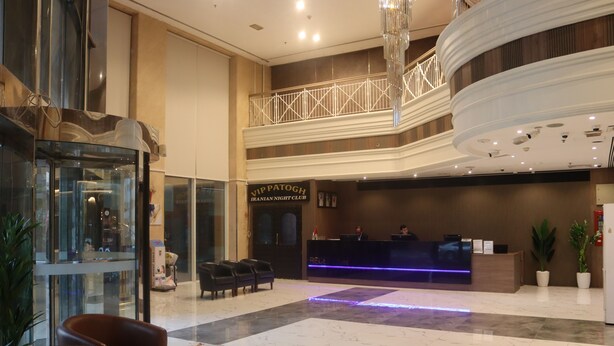 A lobby with a reception desk, seating area, and a glass elevator. - GSS Avenue Hotel (Dubai)