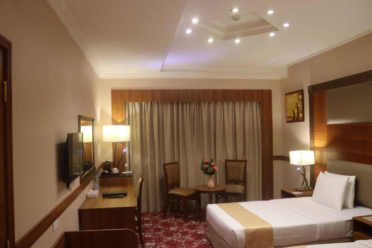 A hotel room with a bed, a desk with a chair, a television, a lamp, and a window with curtains.