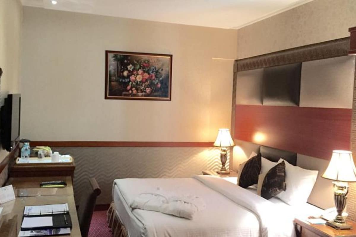 A hotel room with a bed, bedside lamps, a desk with a mirror, a painting on the wall, and a headboard.