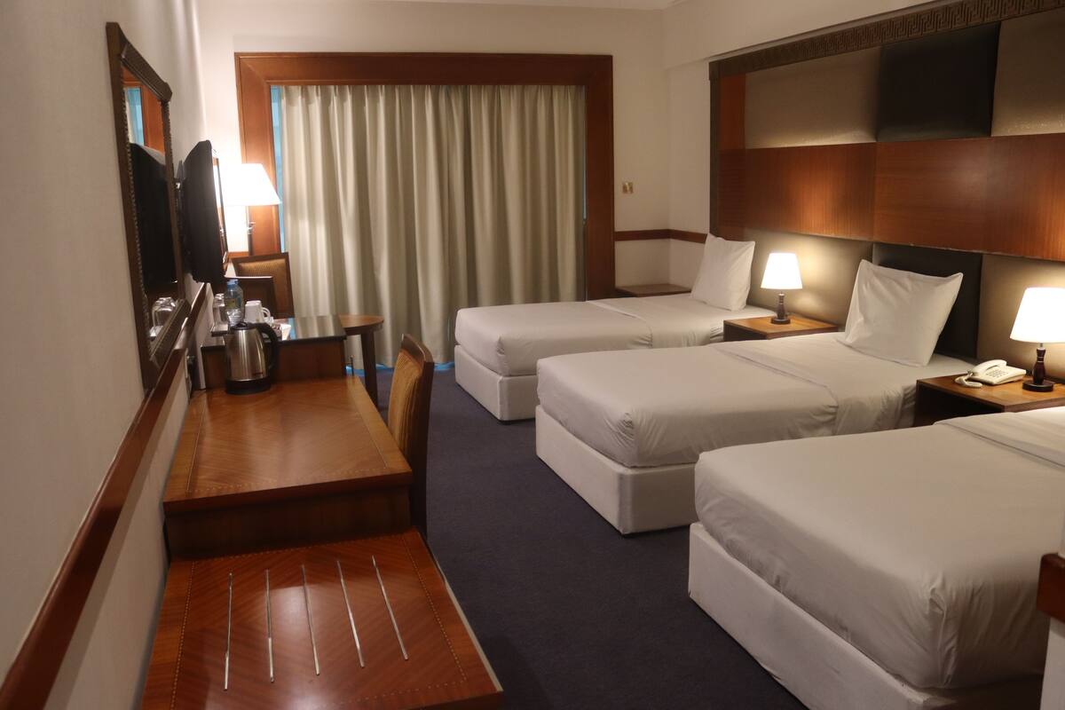 A hotel room with two beds, a desk, a chair, a mirror, a television, and a window with curtains.
