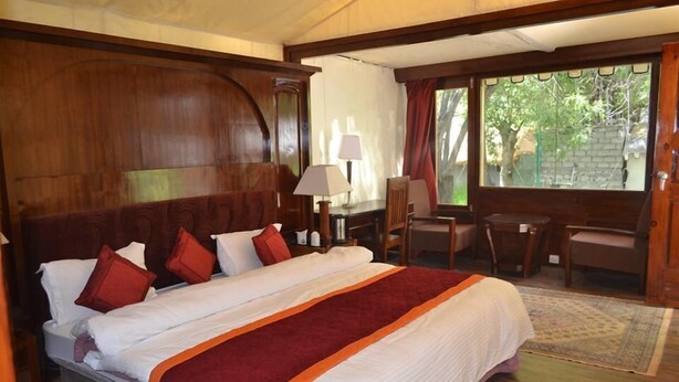 Quarto de hotel com uma cama grande, uma mesa, uma cadeira e janela com vista para o verde.