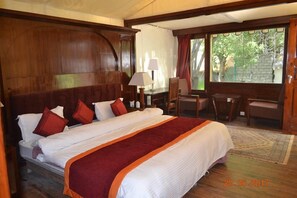 A hotel room with a large bed, a desk, a chair, and a window with a view of greenery. - Turtuk Holidays - Glamping (Leh)