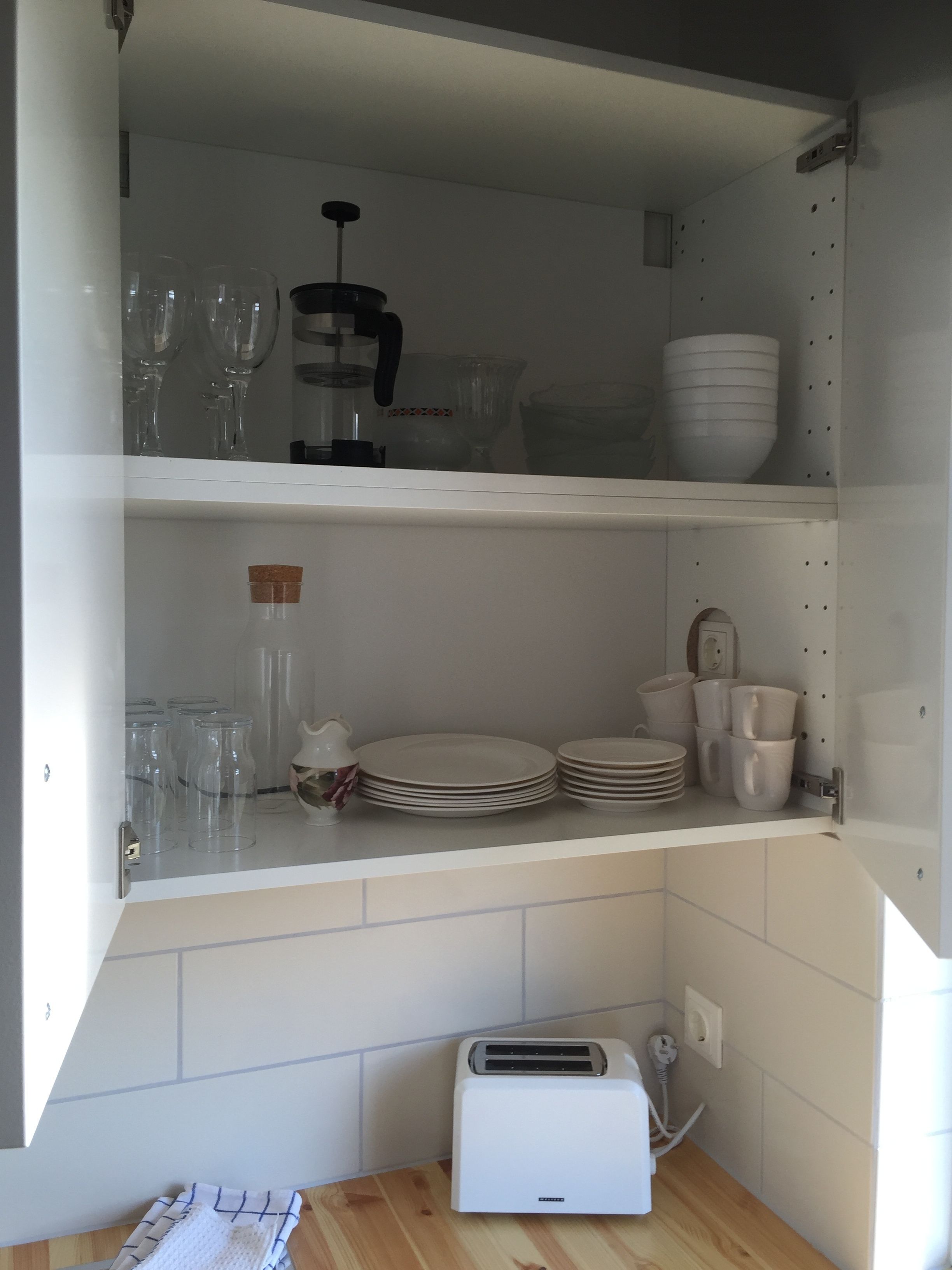 Una cucina con mobili bianchi, un tostapane e diversi piatti e bicchieri.