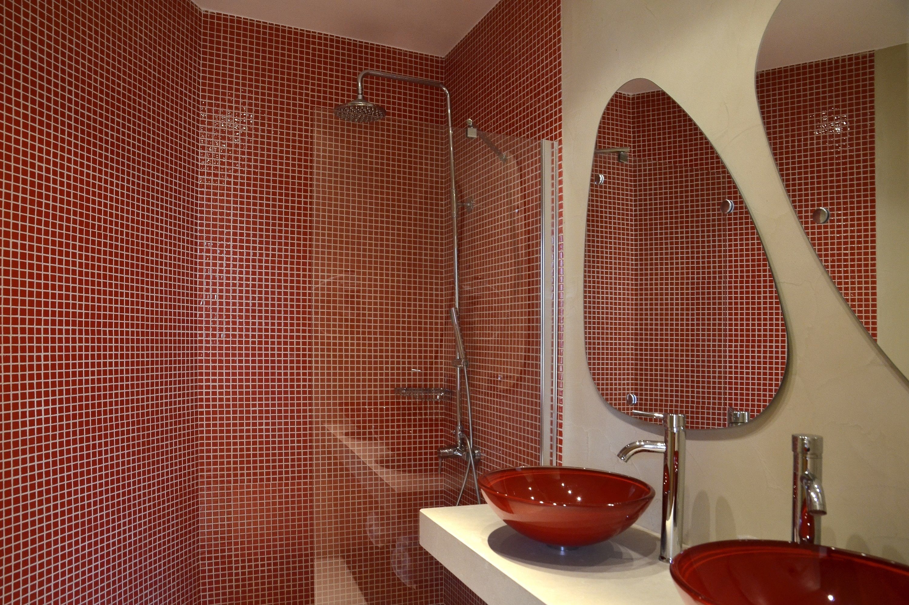 A bathroom with red tiled walls, a shower, and two sinks with red bowls.