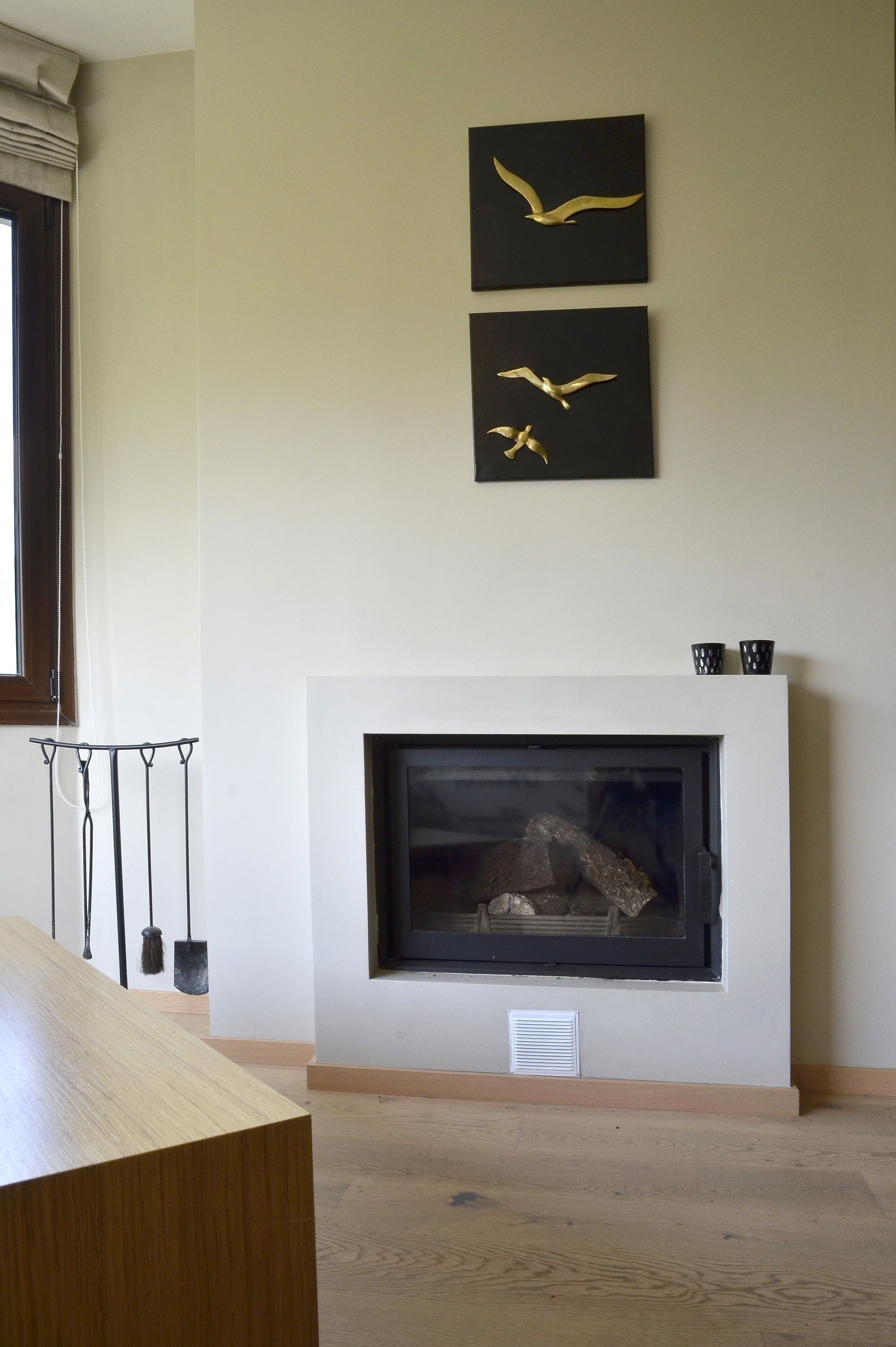 A room with a fireplace, a wooden table, and two wall-mounted bird paintings.