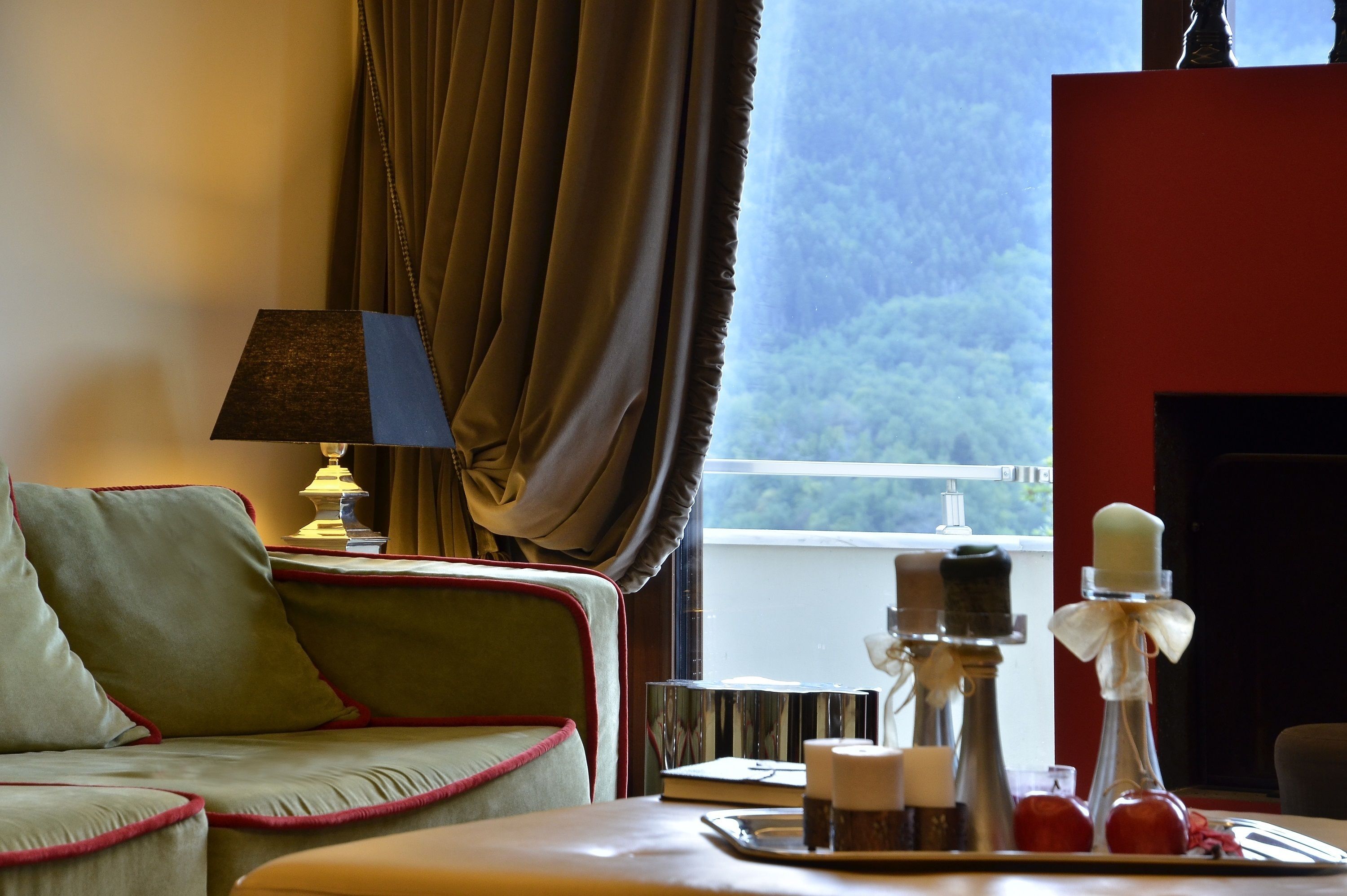 A cozy room with a sofa, a table with candles, a lamp, and a view of greenery outside.