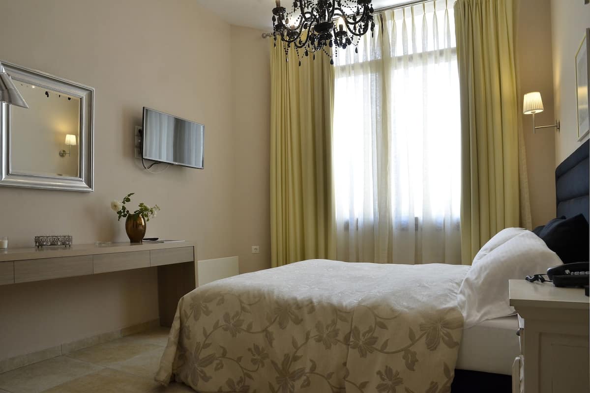 Une chambre d’hôtel comprenant un lit, une table de chevet, une lampe, une télévision et une fenêtre avec des rideaux.