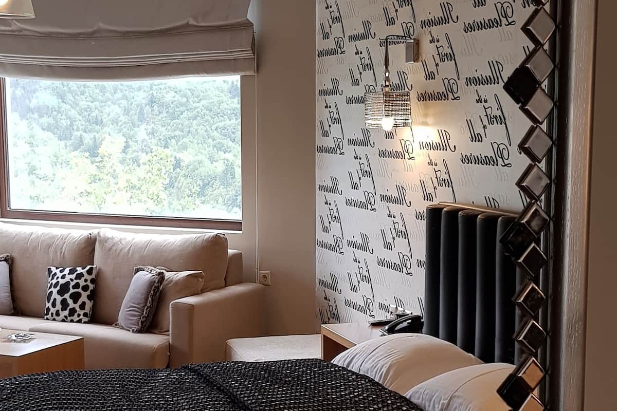 Une chambre d’hôtel avec un lit, un canapé, une fenêtre donnant sur des arbres et un mur orné d’un motif de lettres.