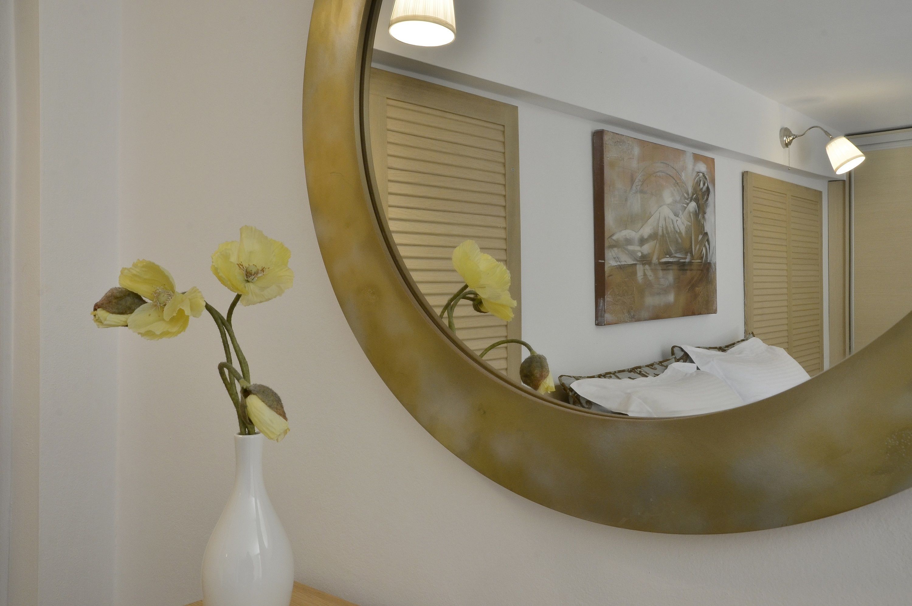 Ein Badezimmer mit einem großen Spiegel, einer weißen Vase mit Blumen und einem Bild an der Wand.