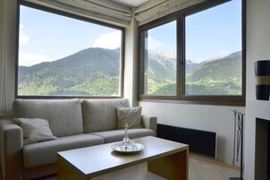 Una sala de estar moderna con un sofá y una mesita de centro, amplias ventanas que ofrecen vistas a la montaña.