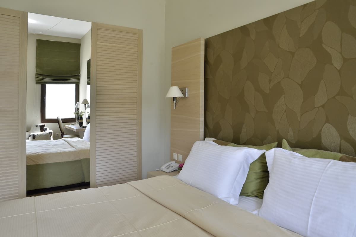 Une chambre d’hôtel avec un lit, une table de chevet avec une lampe, un téléphone et un mur orné d’un motif de feuilles.