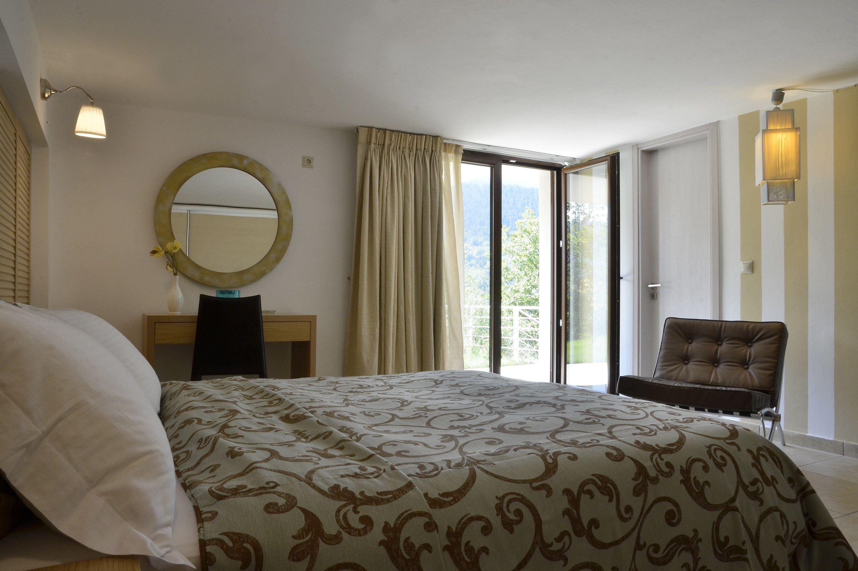 Un dormitorio con una cama grande, un escritorio, una silla, un espejo y vistas al exterior.