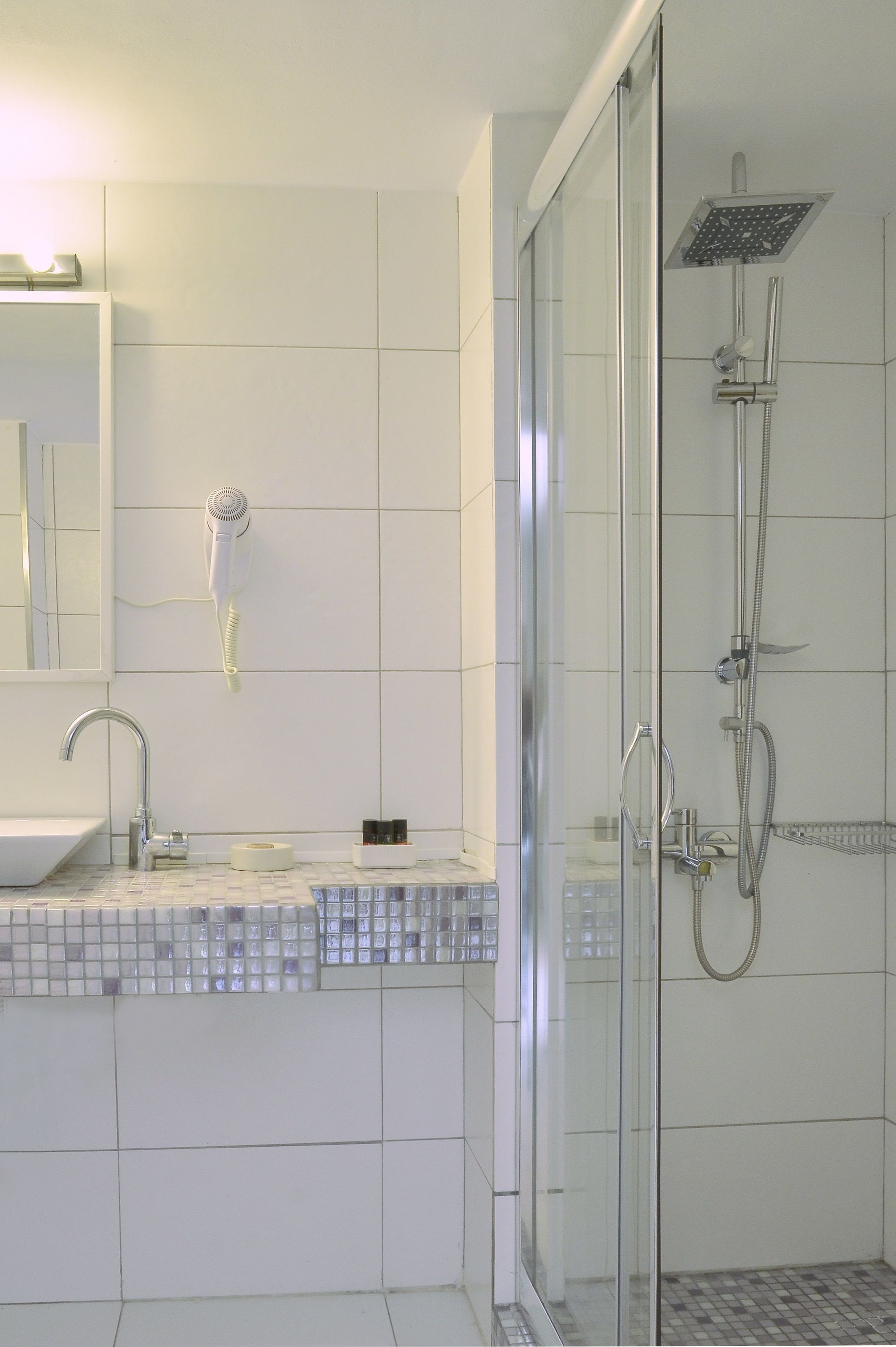 A modern bathroom with a glass shower enclosure, a white sink, and a hairdryer mounted on the wall.