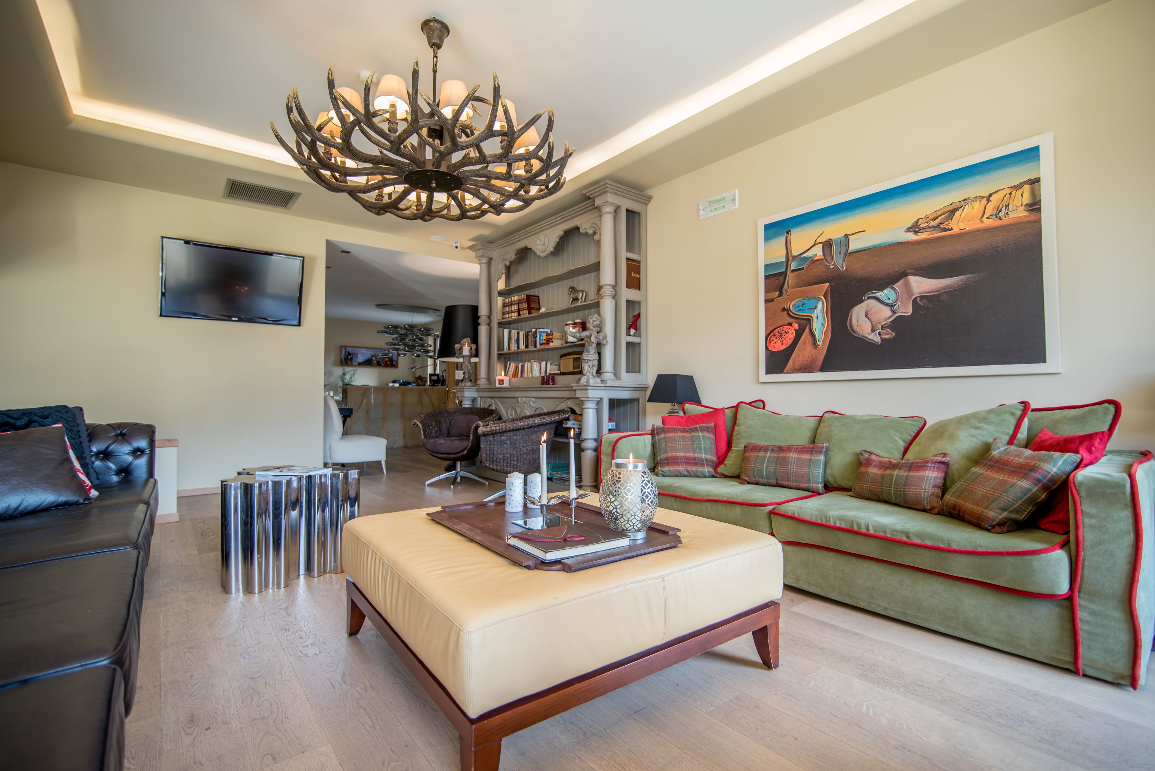 Un salon moderne avec une cheminée, un canapé vert orné de bordures rouges, un fauteuil en cuir et un grand tableau accroché au mur.