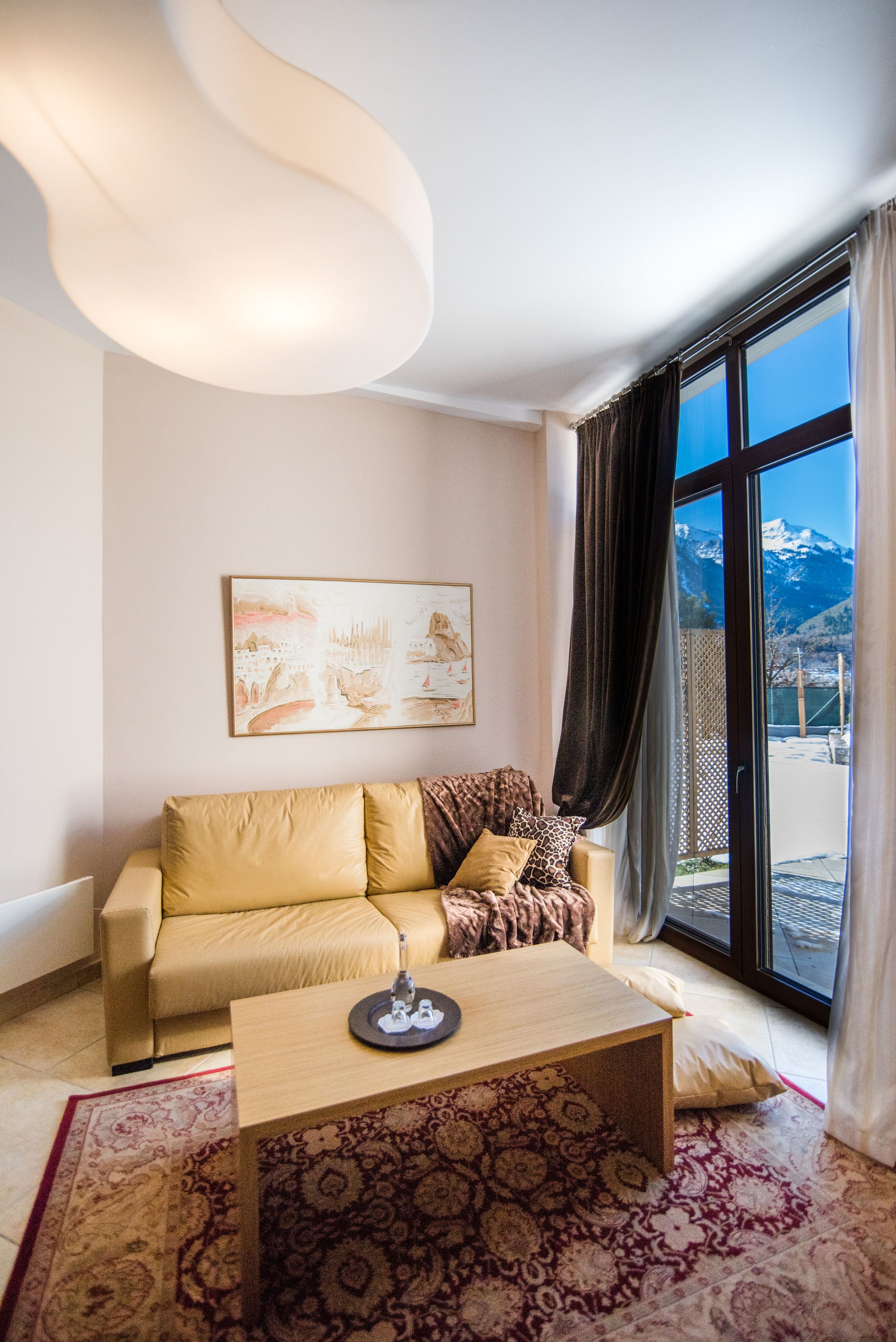 A living room with a sofa, a coffee table, and a large window with a mountain view.