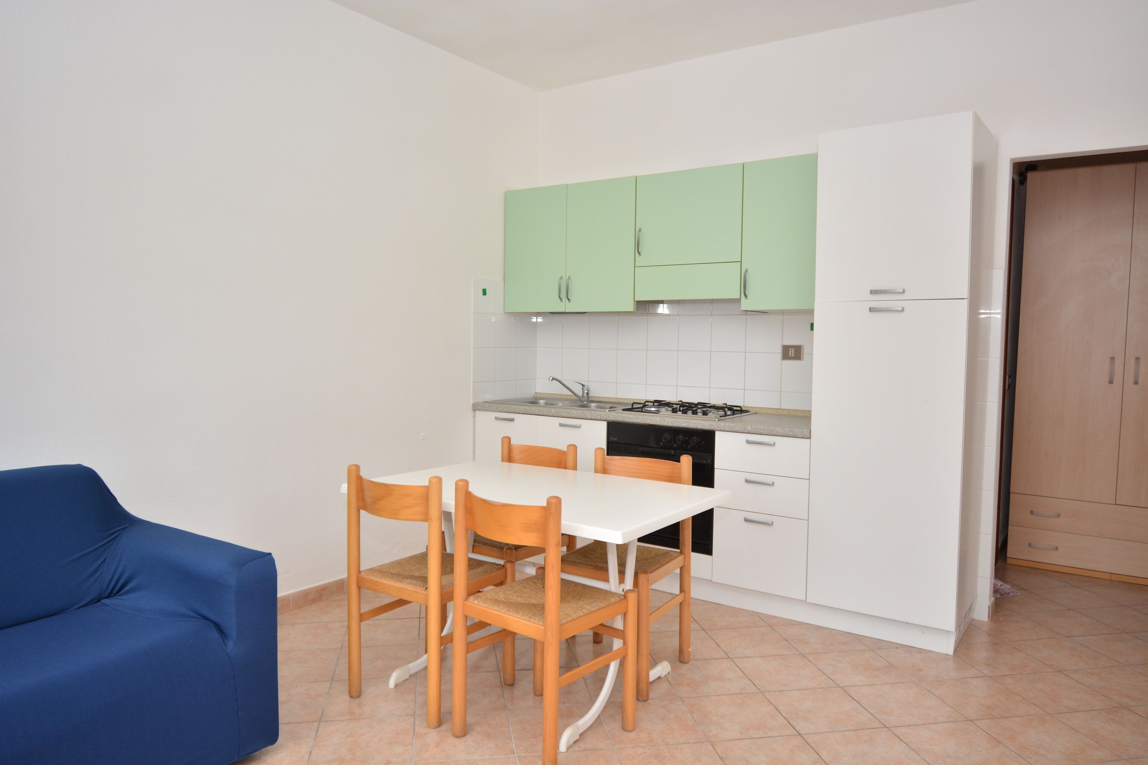 A compact kitchen with a dining table and chairs, a blue sofa, and light green cabinets.