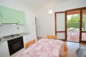 Una cucina compatta con piano cottura e forno a gas, un tavolo con sedie e una porta scorrevole in vetro che dà su un patio esterno con tavolo e sedie.