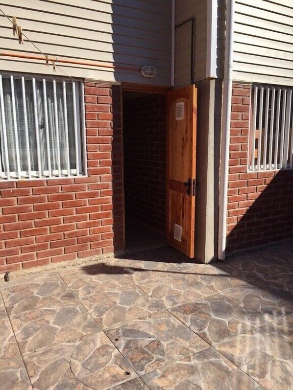 A building entrance with a wooden door, a brick wall, and a window with white bars.