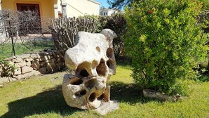 A stone sculpture in a garden with a house in the background. - Granchio Apartment (San Teodoro)