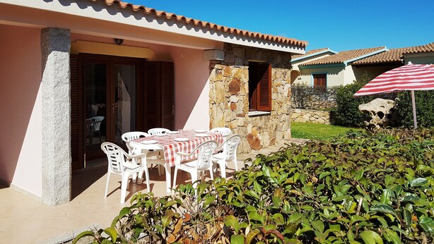 A house with a stone exterior, a tiled roof, and a patio with white plastic chairs and a table. - Granchio Apartment (San Teodoro)
