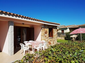 Una casa con fachada de piedra, techo de tejas y un patio con sillas y mesa de plástico blanco.