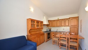 A compact kitchen with wooden cabinets, a stove, and a dining area with chairs. - Granchio Apartment (San Teodoro)