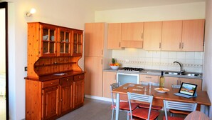 A kitchen with wooden cabinets, a dining table with chairs, a stove, and a tablet on the table. - Granchio Apartment (San Teodoro)
